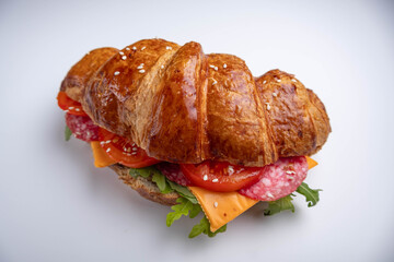 Croissant sandwich with cheese, meat and arugola on white wooden table