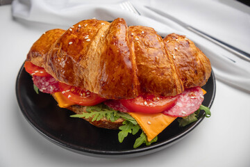 Croissant sandwich with cheese, meat and arugola on white wooden table