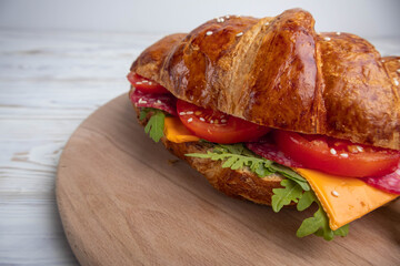Croissant sandwich with cheese, meat and arugola on white wooden table