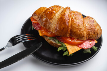 Croissant sandwich with cheese, meat and arugola on white wooden table