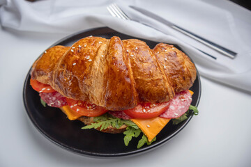 Croissant sandwich with cheese, meat and arugola on white wooden table