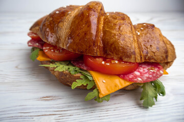 Croissant sandwich with cheese, meat and arugola on white wooden table