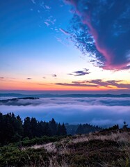 Fototapeta premium Sunrise over a sea of clouds, with a mountain vista. Lush forest draped in the early morning mist