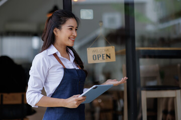 Female cafe owner wearing an apron, showing confidence in her small business, stands in front of...