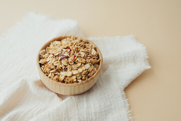 Granola in wooden bowl on soft white textile top view