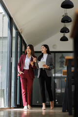 Two Entrepreneur Asian business women discussing new business project in tablet in modern Meeting...