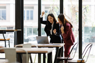 Two excited happy Young Asian businesswomen discuss with new startup project Idea presentation, analyze planning and financial statistics and investment market at office.
