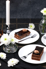 Decadent chocolate cakes with cream and flowers on dark table beside candle