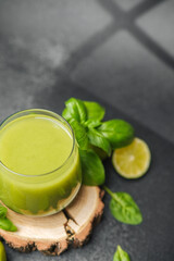 Glass of green smoothie with basil and lime on rustic wood slice dark backdrop