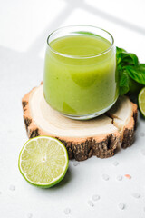Green smoothie in glass with lime and basil leaves on wooden slice on white surface