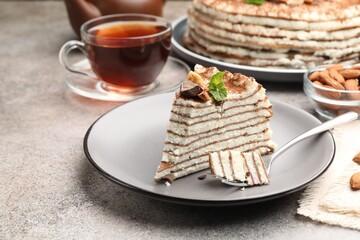 Piece of tasty crepe cake with cocoa powder, chocolate and nuts served on light table, closeup
