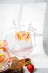 Strawberry lemon infused water in pitcher and glasses served with ice cubes and fresh fruit