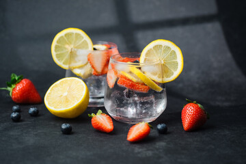 Sparkling lemonade with lemon slices strawberries and blueberries in glass on dark background with...