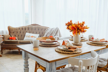 Warm autumn dining table setting with pumpkins and colorful maple leaves indoors.