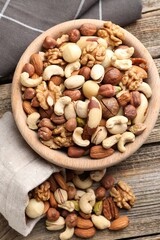 Mix of different nuts in bowl and bag on wooden table, top view
