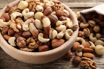 Mix of different nuts in bowl and bag on wooden table, closeup