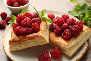 Yummy puff pastries with raspberries and mint on wooden table, closeup