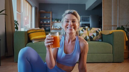 Smiling senior woman in sportswear relaxing and drinking healthy juice after exercising on yoga mat at home, promoting healthy lifestyle and wellness in later years