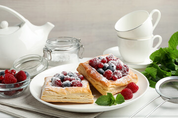 Tasty puff pastries with berries, powdered sugar and mint on white table, closeup