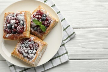 Tasty puff pastries with berries, powdered sugar and mint on white wooden table, top view. Space for text