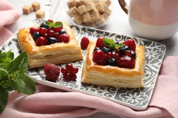 Tasty puff pastries with berries, mint and brown sugar on table, closeup