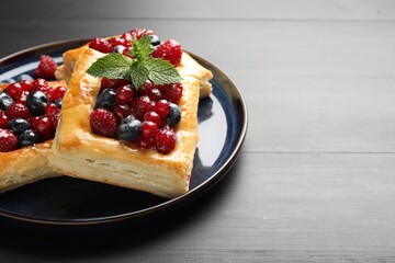 Tasty puff pastries with berries and mint on grey wooden table, closeup. Space for text
