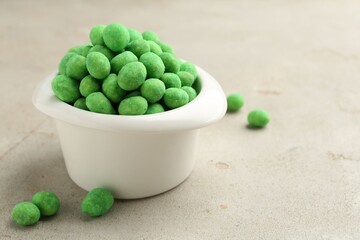 Wasabi coated peanuts in bowl on light table, closeup. Space for text