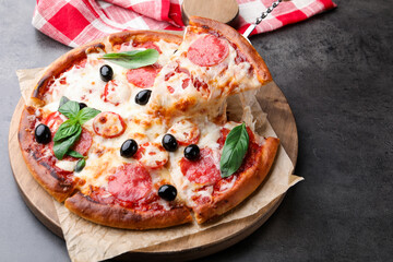 Taking piece of delicious pizza with cheese, salami, olives and basil at grey table, closeup