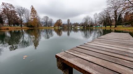 Serene autumn landscape with calm pond, rustic wooden dock, vibrant orange and yellow trees, overcast sky, and tranquil water reflections with copy space on the right