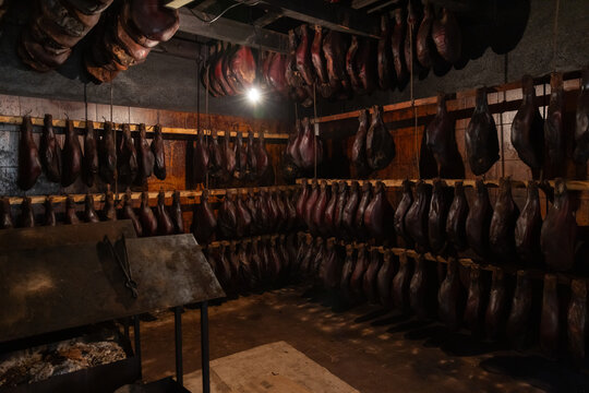 Interior scene of a dark meat-curing cellar with rows of hams