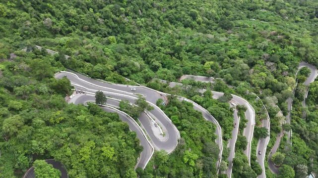 Wide shot showing the early, curvy sections of the Kolli Hills 70-hairpin road. The road crosses farmed red-soil land before entering the dense forest slopes.