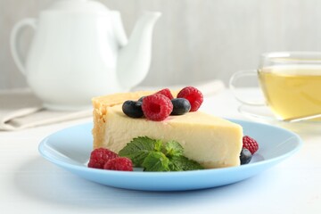 Piece of delicious cheesecake with fresh berries and mint served on white table, closeup