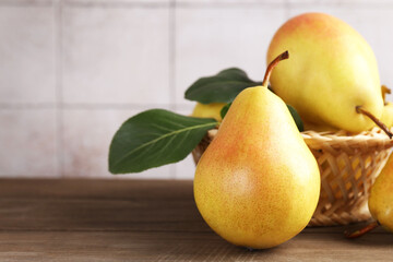 Fresh pears with green leaves and wicker basket on wooden table against light grey tiled wall, closeup. Space for text