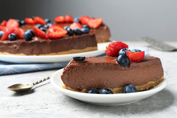 Piece of tasty chocolate cheesecake with berries on light grey textured table, closeup