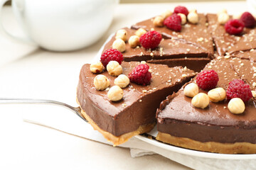 Taking piece of delicious chocolate cheesecake with nuts and raspberries at beige table, closeup