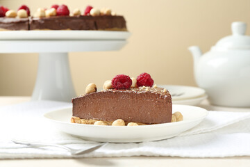 Piece of delicious chocolate cheesecake with nuts and raspberries on beige table, closeup
