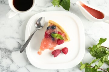 Piece of tasty cheesecake with berries and sauce served on white marble table, flat lay