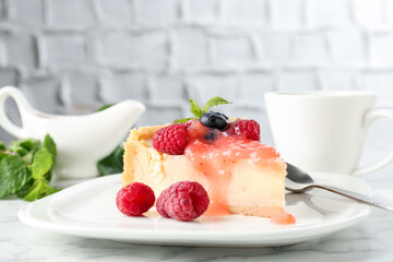 Piece of tasty cheesecake with berries and sauce served on white marble table, closeup
