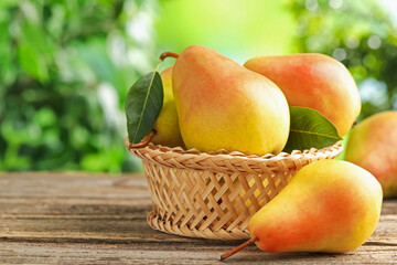 Fresh ripe pears in wicker basket on wooden table outdoors, closeup. Space for text