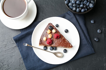 Piece of delicious chocolate cheesecake with nuts, berries and tea on black table, flat lay