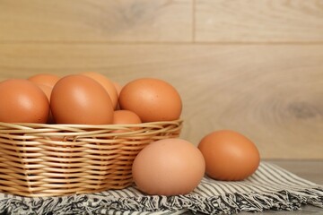 Raw chicken eggs in wicker basket on wooden countertop, closeup. Space for text
