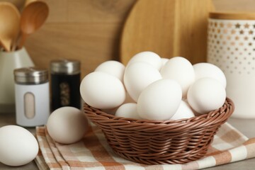 Raw chicken eggs in wicker bowl and kitchen utensils on wooden countertop, closeup