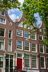 In Amsterdam, the charming facades of colorful houses showcase classic Holland architecture. The buildings feature unique designs and vibrant colors against a bright blue sky.
