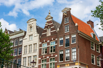 In Amsterdam, the charming facades of colorful houses showcase classic Holland architecture. The buildings feature unique designs and vibrant colors against a bright blue sky.