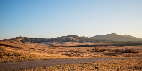 Expansive golden grassland with rolling hills under a clear sky at sunset, conveying a sense of vast open space and tranquility