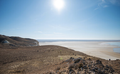 Expansive desert-like landscape under a clear blue sky, featuring rugged hills and a flat, arid plain stretching into the distance, with a calm and tranquil atmosphere.