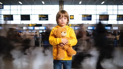 Child stands still with teddy bear in busy airport terminal. Background shows travelers in motion, bright interior with departure signs. Concept of travel, family, emotional support