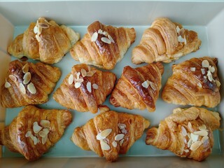Golden baked almond croissant pastries with delicious honey glaze delight senses. box full of freshly made sweet breakfast treats for joyful morning