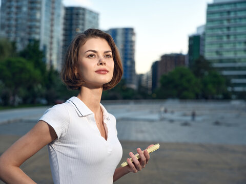A confident woman stands on a sunny urban beach, holding a smartphone as she gazes into the distance. The scene conveys focus, independence, and a modern lifestyle.