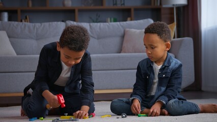 Two African American children playing with plastic toys at home brothers ethnic kids sons boys siblings friends play game repair on floor building with hammer friendship family childhood playtime